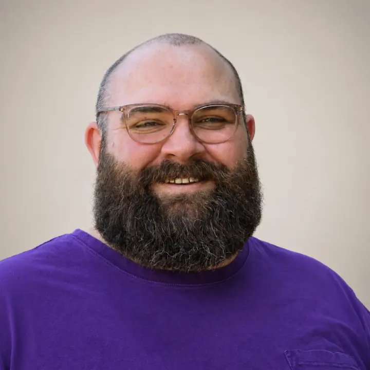 Richard Couch smiling, wearing glasses and a purple shirt